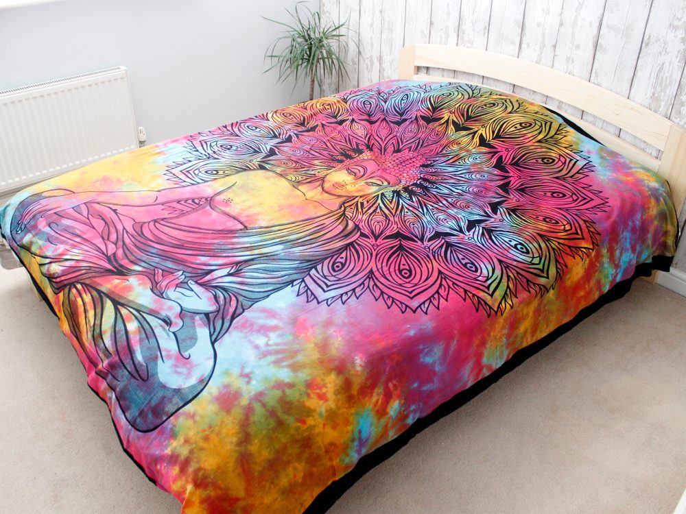 A tie-dye tapestry depicting a meditating Buddha within a mandala rests on a bed in a bedroom.