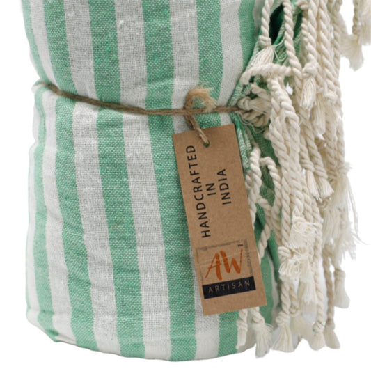 A mint green and white striped towel is rolled and tied with twine. It has off-white fringe and a tag reading “HANDCRAFTED IN INDIA” and “AW ARTISAN”.
