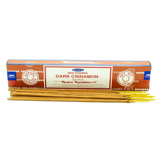 Incense sticks, labeled "Satya Nag Champa Dark Cinnamon," lie beside an orange box with export quality branding. It reads: "Shrinivas Sugandhalaya LLP" and "NET. WT. 15g."