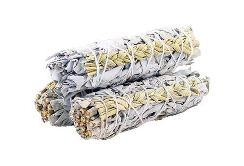 Three bundles of dried, silvery-green sage are stacked; the stems are wrapped with white string, and they are in a bright, white space.
