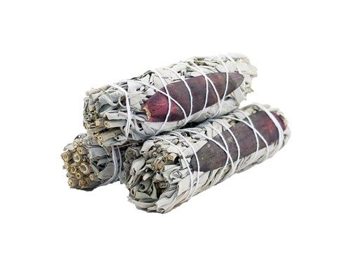 Three wrapped bundles of white sage and dragon's blood sit stacked on a white surface. The sage is arranged around a dark red center and bound with white string.