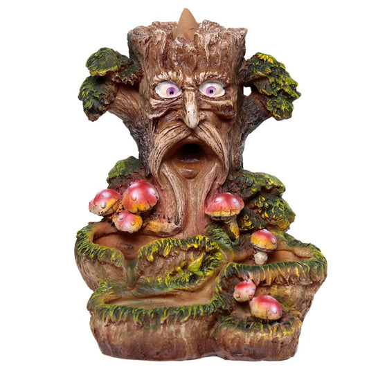 A tree-shaped sculpture with a face, wide eyes, and open mouth appears surrounded by small red mushrooms and green foliage, conveying an animated, whimsical forest scene.