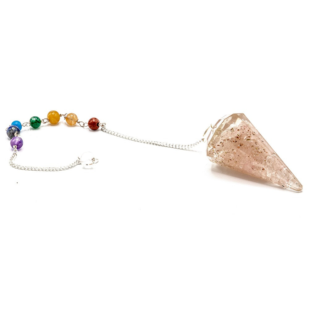 A pendulum with a pink-toned quartz crystal point and a chain ending with chakra-colored beads lies on a white surface.