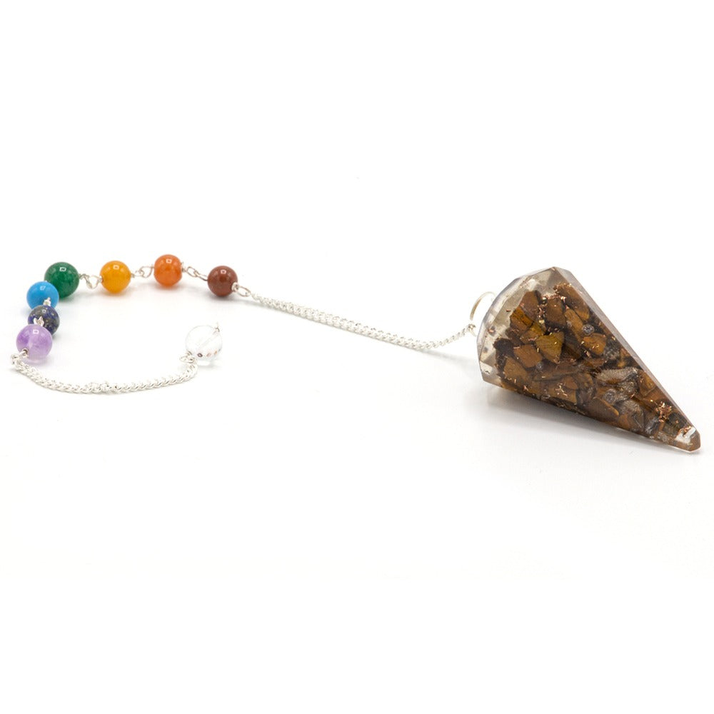 A pendulum with tiger's eye embedded in resin, hangs from a silver chain ending in rainbow-colored chakra beads on a white background.