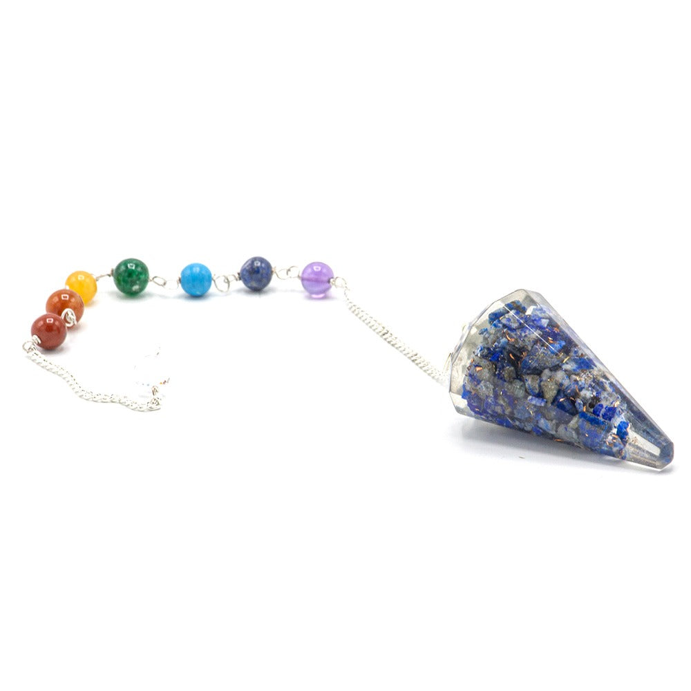 A pendulum lays against a white background; the weight, a clear cone encapsulating blue stones, is connected by a silver chain to colored beads.
