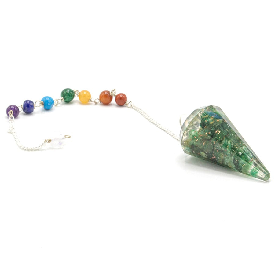 A green, cone-shaped pendulum lays on a white surface. A silver chain connects the pendulum to a string of colorful beads.
