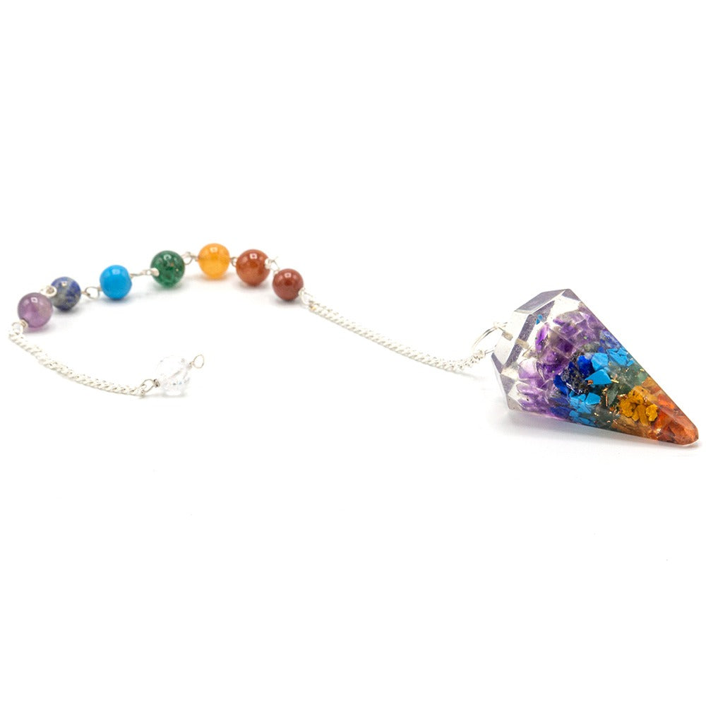 A chakra pendulum with cone-shaped crystal pendant and colorful beads is suspended by a silver chain against a white background.