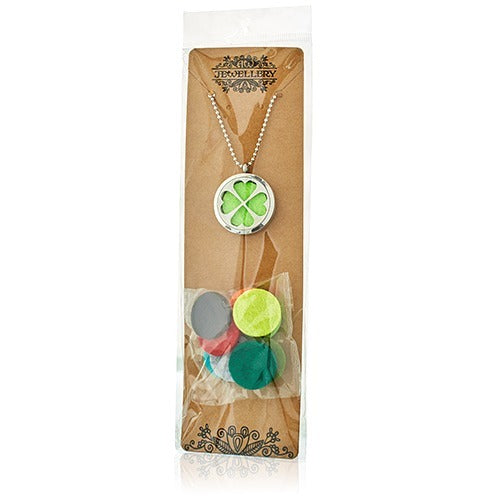 A four-leaf clover aromatherapy necklace hangs on a brown card, accompanied by several colorful felt pads. JEG JEWELLERY is printed on the card.