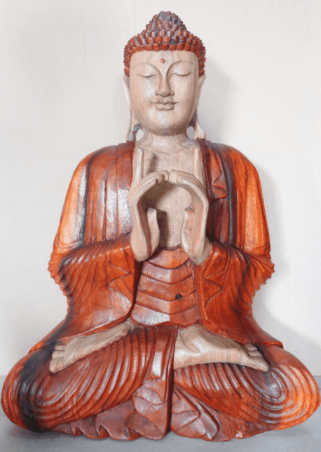 A wooden Buddha statue, seated in a meditative posture with hands forming a gesture, is set against a plain background. The robe features intricate carving details.