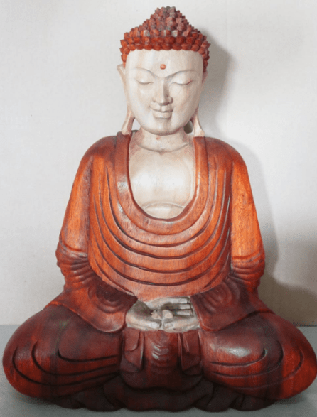 A wooden Buddha statue sits in meditation, hands resting in lap, adorned in detailed robes, against a plain background.