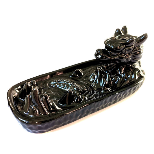A glossy black ceramic dragon-shaped incense holder sits with its head raised, surrounded by wave-like patterns on its base, set against a plain white background.