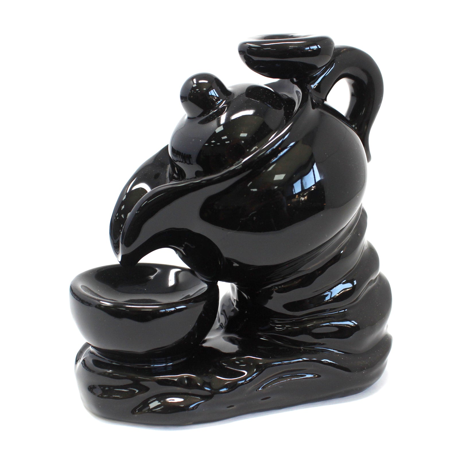 A black ceramic teapot pours into a matching bowl, set on a wavy, sculpted base, creating an artistic, fluid design.