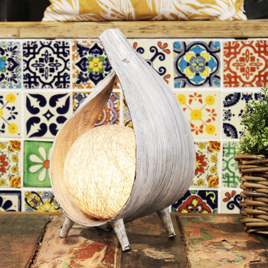 A gray wooden lamp, holding a lit globe, sits on a rustic table against a colorful tiled wall.