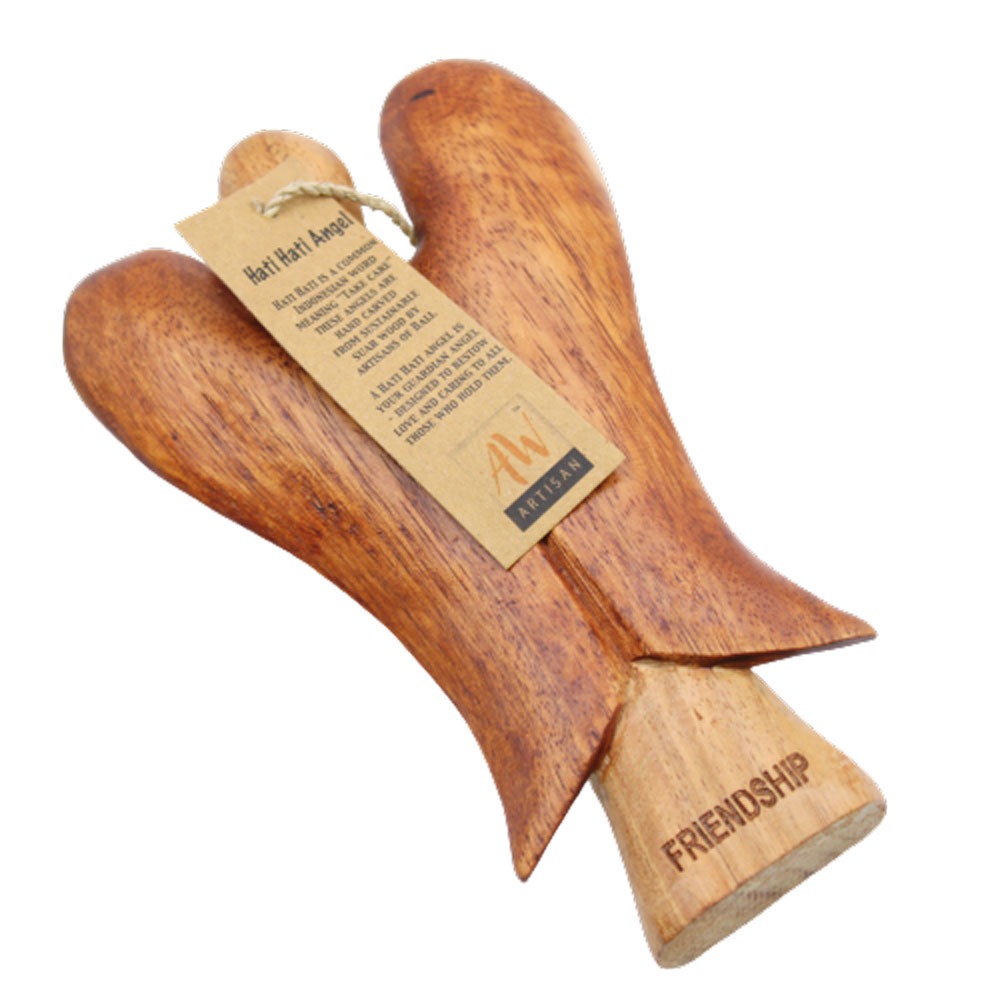 A wooden angel ornament has an attached tag and the word “FRIENDSHIP” etched into its base. The tag contains text that reads “Hati Hati Angel. HATI HATI IS A COMMON INDONESIAN WORD MEANING “TAKE CARE." THESE ANGELS ARE HAND CARVED FROM SUSTAINABLE SUAR WOOD BY ARTISANS OF BALL. A HATI HATI ANGEL IS YOUR GUARDIAN ANGEL DESIGNED TO BESTOW LOVE AND CARING TO ALL THOSE WHO HOLD THEM”.