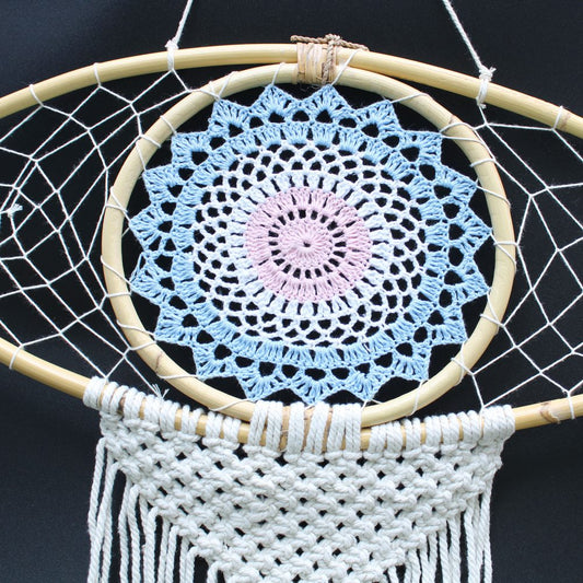 A crocheted mandala is affixed to a bamboo dream catcher, hanging against a dark background.