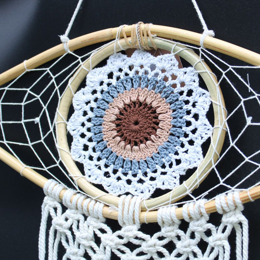 A crocheted mandala hangs from a wooden dreamcatcher; a neutral background surrounds it.