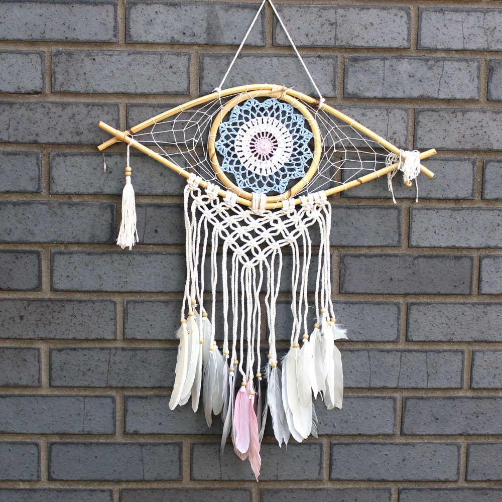 A dreamcatcher hangs against a brick wall. It features a crocheted mandala and feathers.
