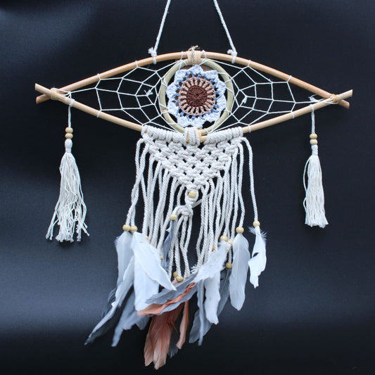 A dreamcatcher hangs against a dark background. It features a wooden frame, woven netting, crocheted center, macrame detailing, and feathers.
