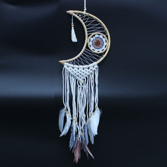 A crescent moon-shaped dreamcatcher, woven with white string and featuring feathers, hangs against a dark background.