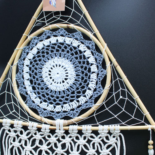A crocheted mandala hangs from a triangular macrame dreamcatcher. The dreamcatcher has wooden dowels, and the mandala is grey and white.