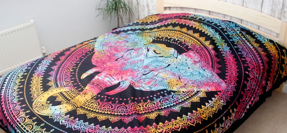 A multicolored elephant design is printed on a tapestry, resting on a bed in a bedroom.