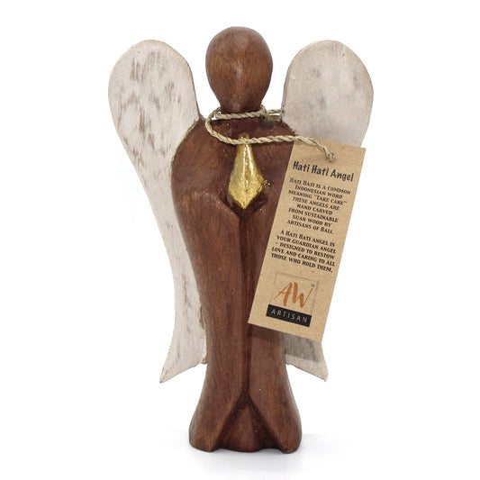 Wooden angel figurine stands on a white background wearing white wings, a gold pendant, and a twine tag reading: Hati Hati Angel HATI HATI IS A COMMON INDONESIAN WORD MEANING "TAKE CARE" THESE ANGELS ARE HAND CARVED FROM SUSTAINABLE SUAR WOOD BY ARTISANS OF BALI. A HATI HATI ANGEL IS YOUR GUARDIAN ANGEL DESIGNED TO BESTOW LOVE AND CARING TO ALL THOSE WHO HOLD THEM. AW ARTISAN