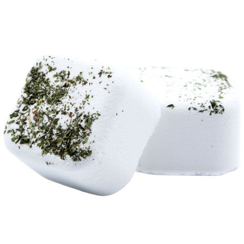 Two white bath bombs sit closely together, with dried green herbs sprinkled on top, set against a plain white background.