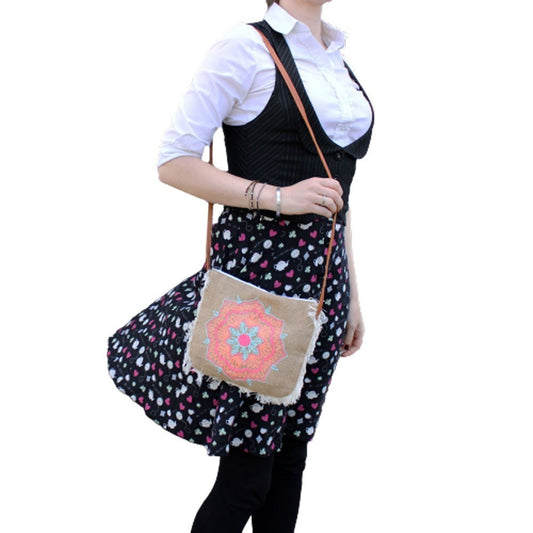 A woman stands, wearing a white shirt, vest, patterned skirt, and tights. She carries a small, embroidered bag across her body with a tan strap. The background is out of focus.