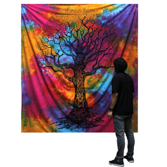A tie-dye tapestry depicting a large tree hangs on a wall; a person observes it.