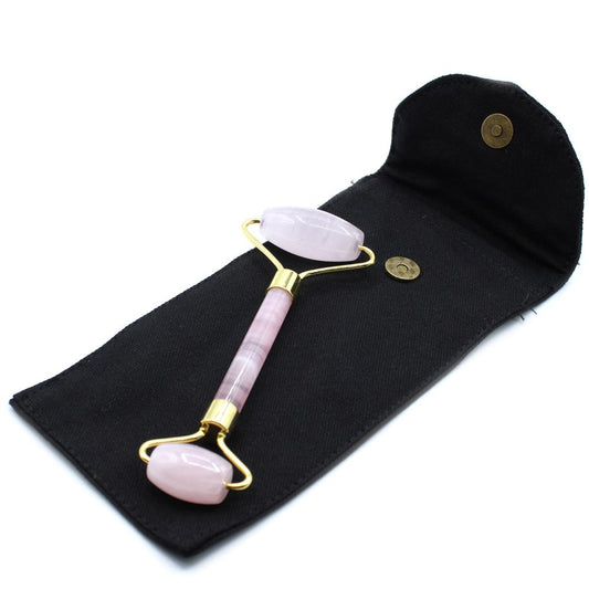 A pink gemstone roller, with gold connectors, rests inside a black, open pouch with a brass clasp. The pouch sits on a white background.