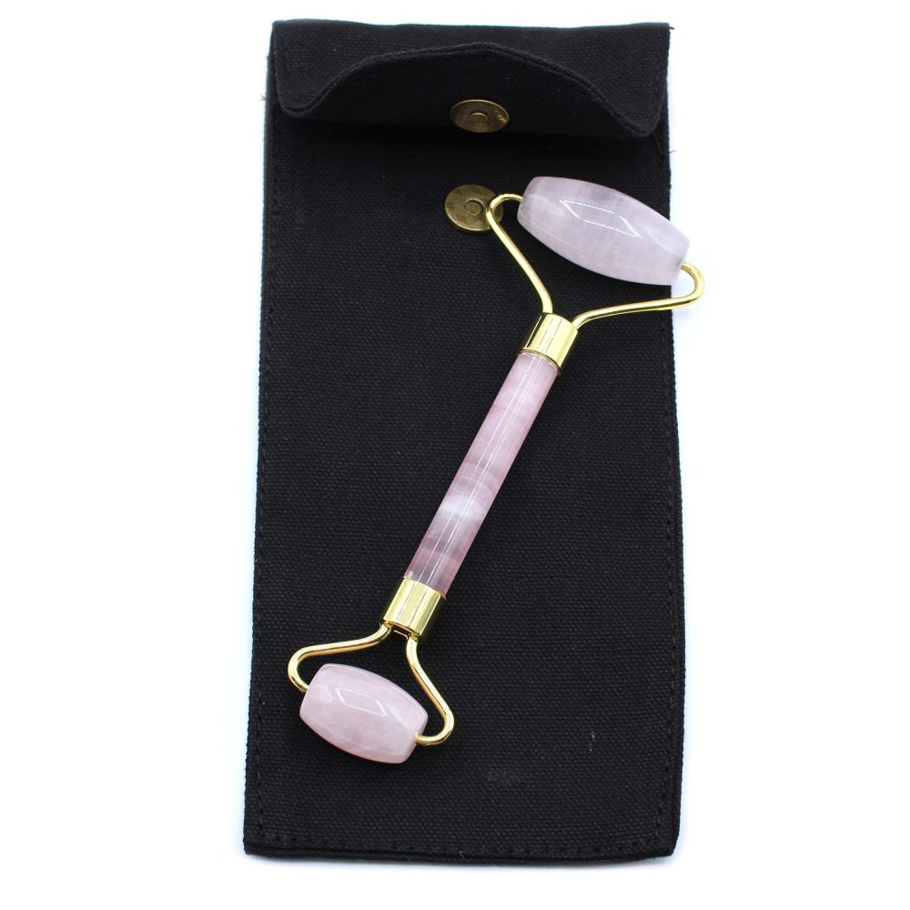 A pink face roller, complete with a gold frame and gemstone ends, sits on top of a black carrying bag with a gold snap, against a white background.