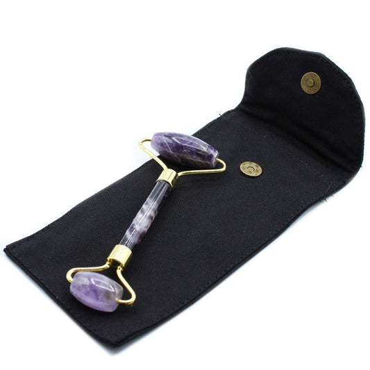 An amethyst face roller rests diagonally across a black fabric pouch with an open flap secured by a visible bronze-colored magnetic snap.