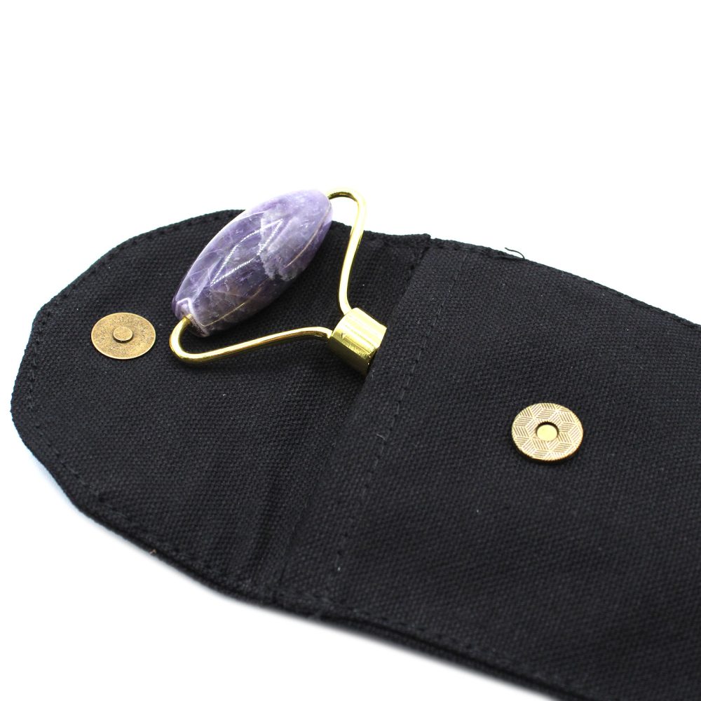 Amethyst roller sits nestled in an opened, black canvas pouch with two gold-colored snap fasteners against a white background.