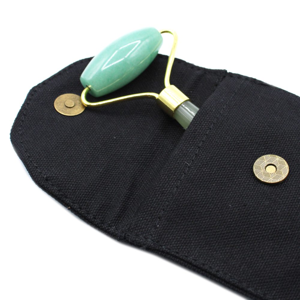 A green jade roller lies in a partially open black pouch. Two golden magnetic buttons, one on each side, secure the pouch.