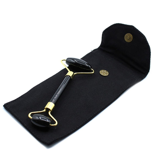 A black facial roller with gold hardware is shown in a black pouch with two bronze snaps, set against a white background.