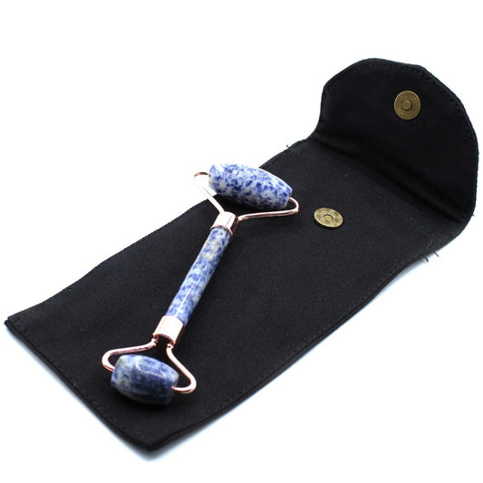 A blue and white stone face roller with rose gold accents rests diagonally on a black, open, snap-closure pouch. The background is solid white.