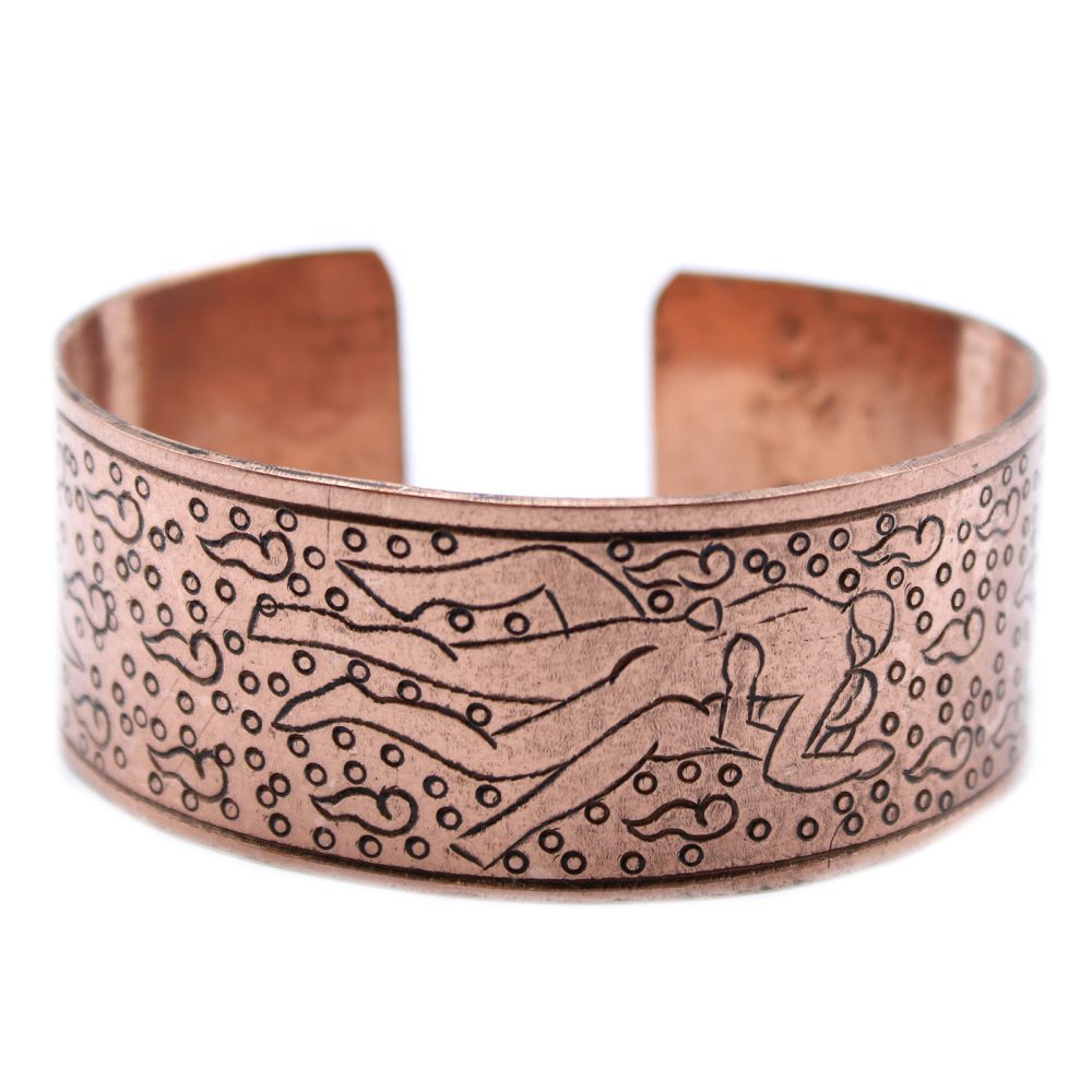 A copper-colored cuff bracelet features an etched design of two reclining figures surrounded by decorative dots on a white background.