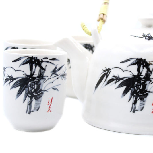 A white teapot and cups, adorned with black bamboo paintings, rest closely together. Their smooth ceramic surfaces display delicate artistry. Red calligraphy contrasts subtly with the bamboo designs.
