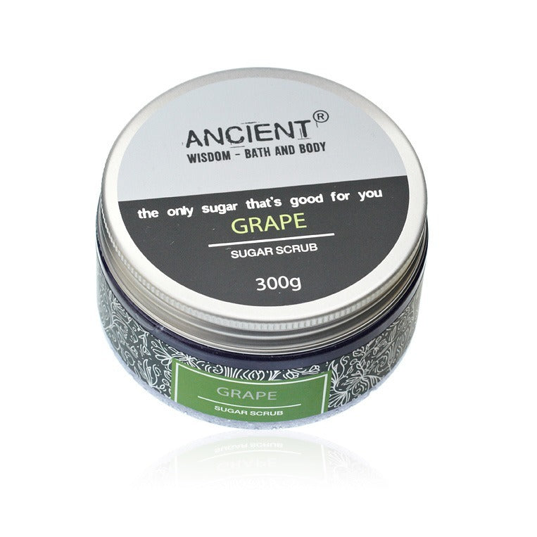 A 300g jar of grape sugar scrub sits on a white reflective surface. The label reads: "ANCIENT, WISDOM - BATH AND BODY, the only sugar that's good for you, GRAPE, SUGAR SCRUB."