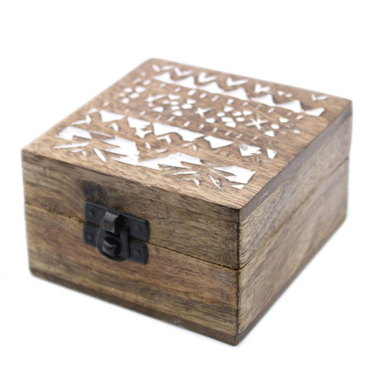 A wooden box with a metal latch features decorative geometric carvings on its lid, placed in a plain setting.