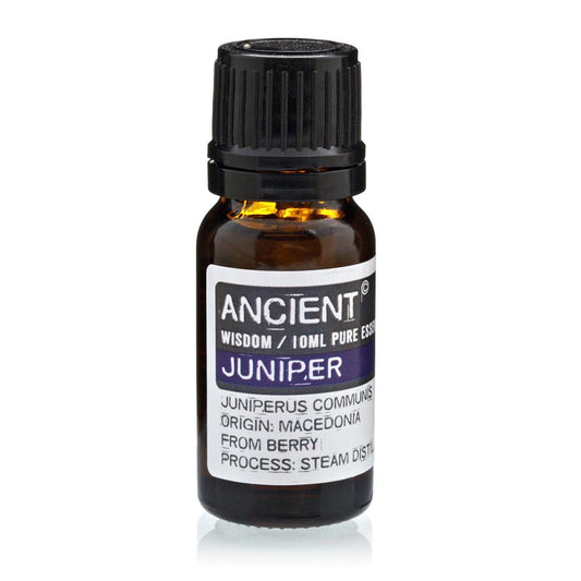 A small brown bottle stands upright, capped with a black ribbed lid. A white label reads: "ANCIENT WISDOM / IOML PURE ESSE JUNIPER JUNIPERUS COMMUNIS ORIGIN: MACEDONIA FROM BERRY PROCESS: STEAM DISTU." The background is plain white.