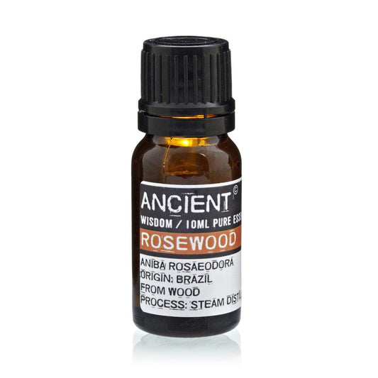 A small amber bottle of "ANCIENT WISDOM / 10ML PURE ESS ROSEWOOD" sits on a white surface. The label states "ANĪBĀ ROSAEODORA ORIGIN: BRAZIL FROM WOOD PROCESS: STEAM DIST".