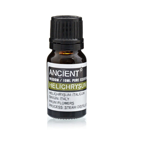 A bottle sits on a reflective surface. The label reads: "ANCIENT, WISDOM / 10ML PURE ESSENTI, HELICHRYSUM, HELICHRYSUM ITALICUM, ORIGIN: ITALY, FROM FLOWERS, PROCESS: STEAM DISTILLA"