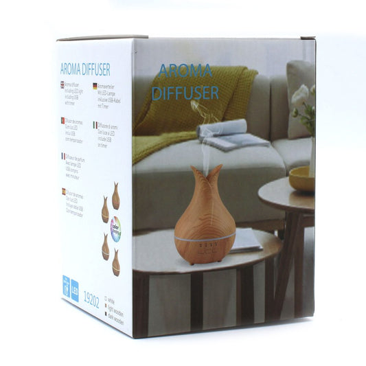 Aromatherapy box with the words “AROMA DIFFUSER” on the left and on the front. The front of the box shows the product – a light wooden aroma diffuser expelling vapor on a table in a living room. The words “white,” “light wooden,” and “dark wooden” appear.