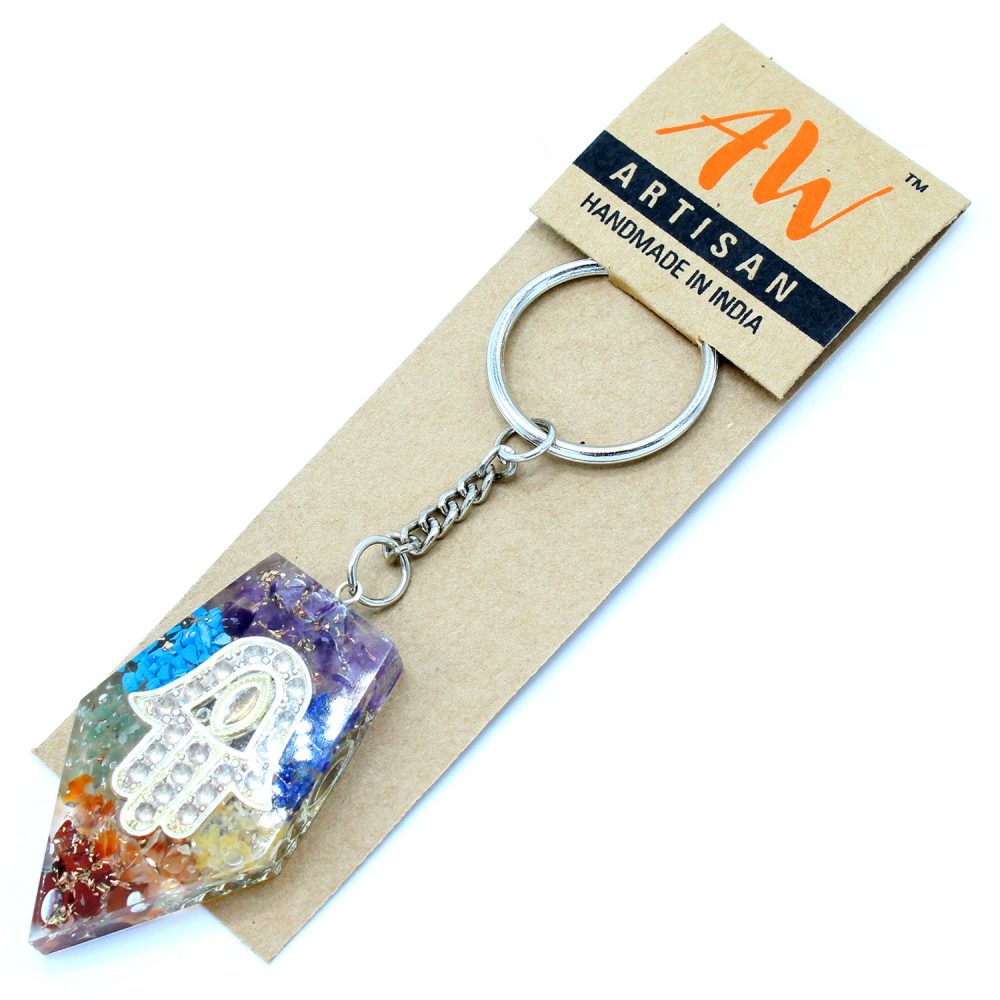 A multi-colored, cone-shaped crystal keychain with a silver Hamsa inlay sits on a cardboard display card labeled: "ARTISAN. HANDMADE IN INDIA." It also has the company’s AW logo on the top right side of the card.