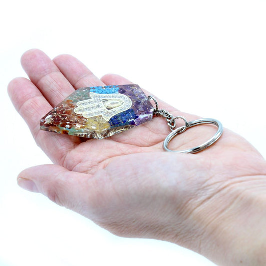 A multicolored gemstone-embedded keychain, adorned with a Hamsa hand, rests in the palm of a hand against a bright white background.