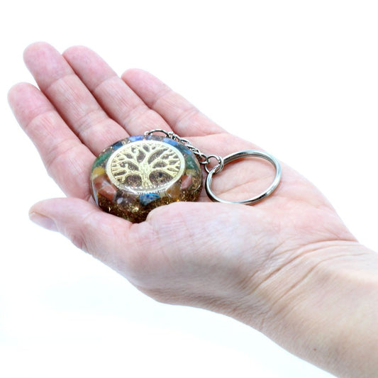A resin keychain, decorated with a golden tree of life, sits in an open palm, displayed in front of a bright white background.