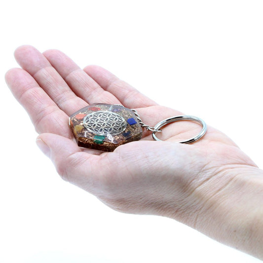 Hand holds a resin keychain with metal flower of life design, and colorful stones embedded within, against a bright, white background.