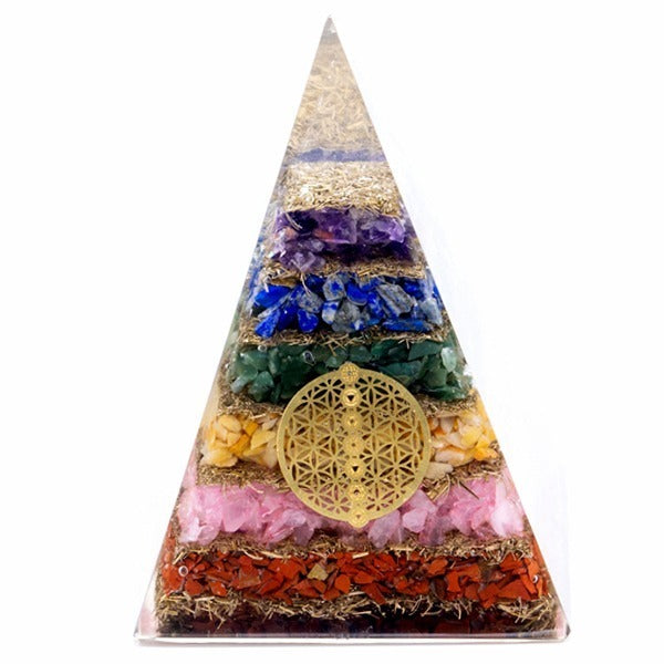 A clear resin pyramid displays layers of red, pink, yellow, green, blue, and purple stones, separated by metallic-looking straw and adorned with a gold geometrical design.