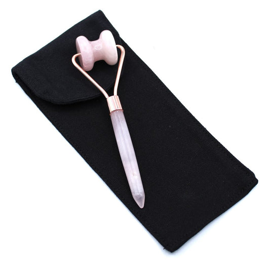 A pink rose quartz facial roller with gold arms lies on a black cloth pouch, all on a white background.